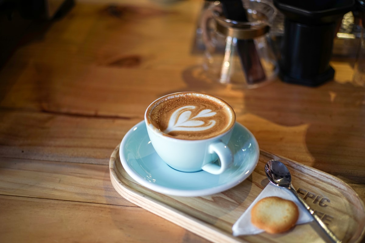 A latte with leaf art in a pale blue ceramic cup on a wooden café tray