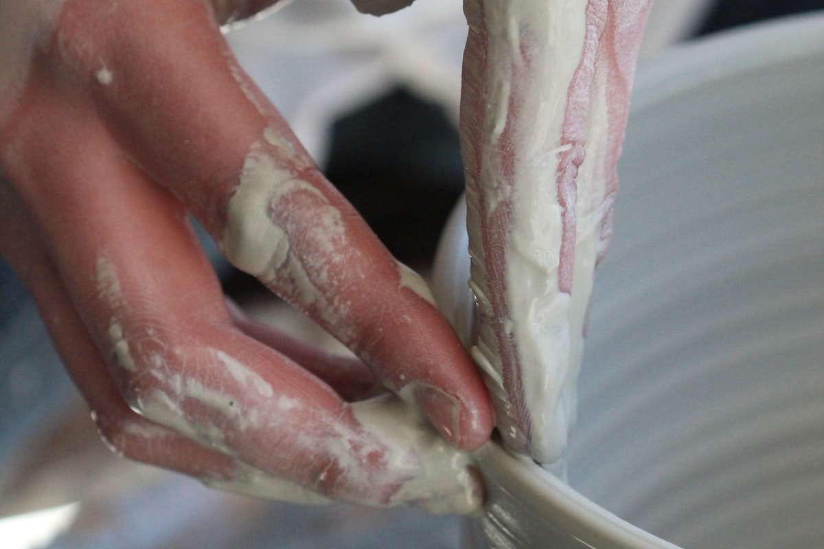 Clay-covered hands shaping a vessel on the pottery wheel