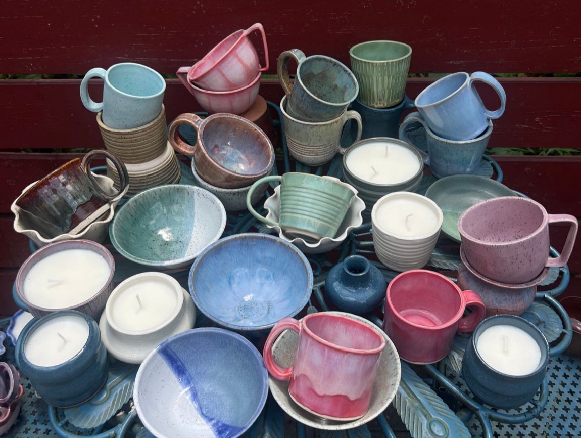 A table crowded with Spindle Lane's handmade mugs, bowls, and candles in soft pinks, blues, and greens